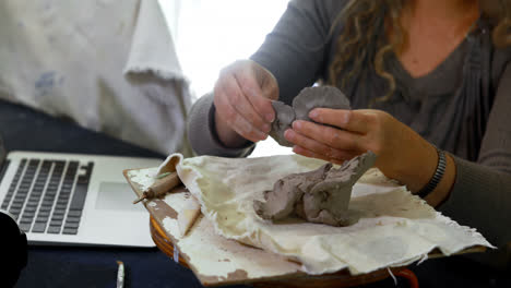 mature female potter molding a clay while using laptop 4k