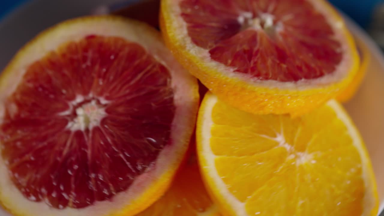 Juicy ripe slices of red and yellow oranges in a white plate slowly rotate