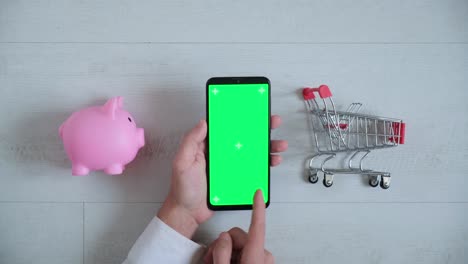 teléfono con una pantalla chromakey en las manos de un primer plano. vista superior de la caja de ahorros del teléfono inteligente y el carrito de compras copia el espacio sobre fondo blanco