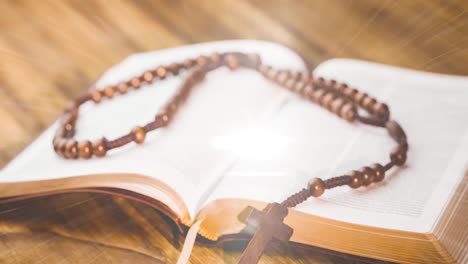 animation of christian rosary on bible with glowing rays on wooden background