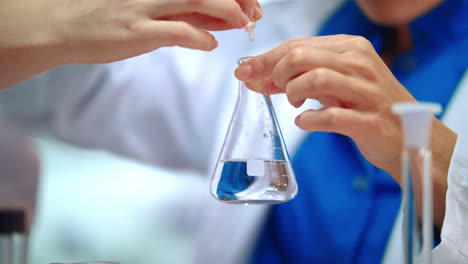 Closeup-of-lab-researcher-hands-dripping-pure-liquid-in-lab-flask