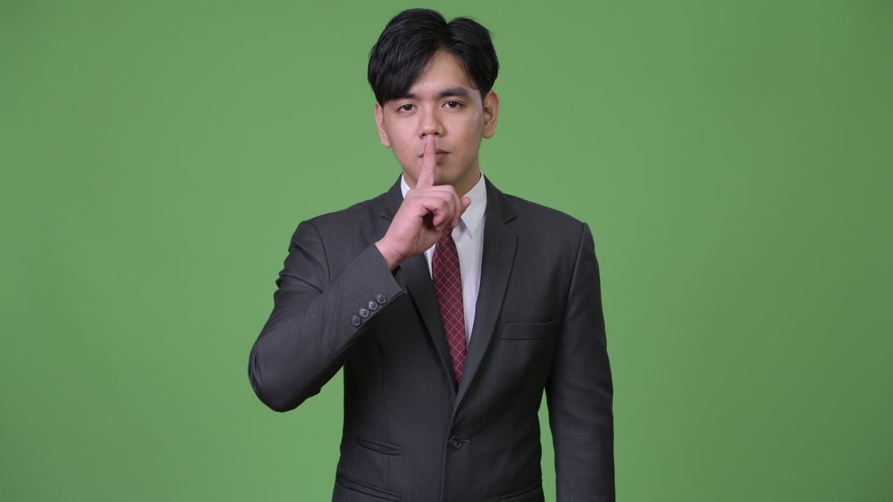 입술에 손가락을 은 젊은 잘생긴 아시아 사업가