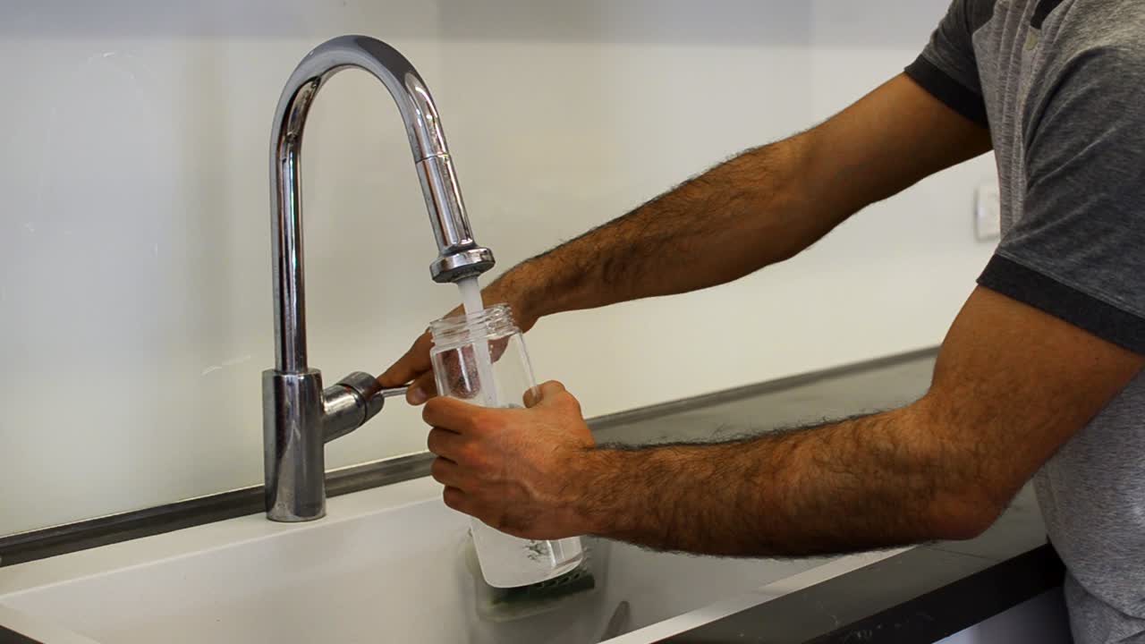 una foto fija de un tipo llenando una botella de agua del grifo al lado del mostrador