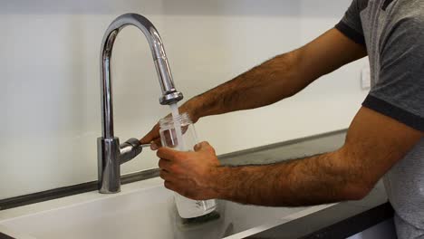 a still shot of a guy filling up a water bottle from the tap next to the counter