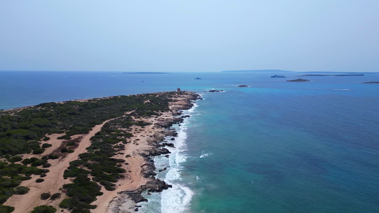 Turquoise waves crashing on the rocky coast of Ses Salines beach with the ancient watchtower. Amazing aerial view flight panorama overview drone