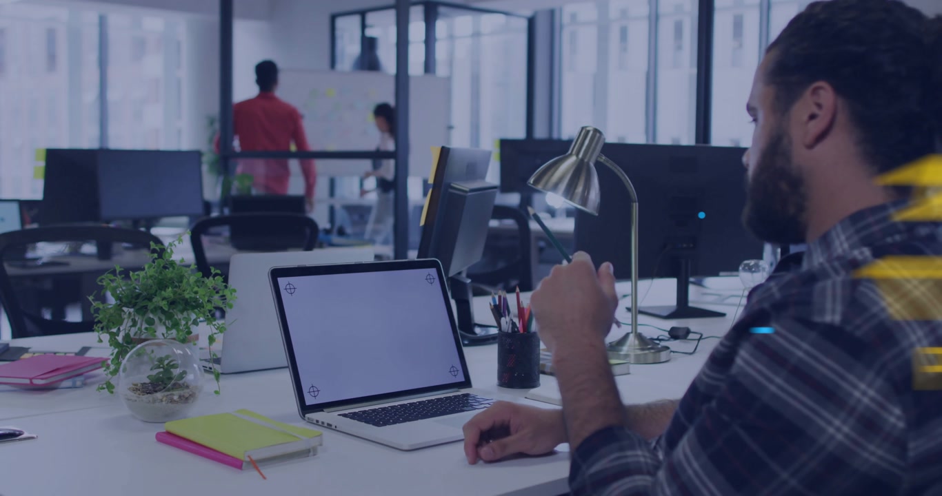 IT pro raising hand above laptop, guiding neon letters orbiting as coworker walking past partition