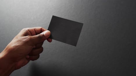 hand of biracial man holding black business card on grey background, copy space, slow motion