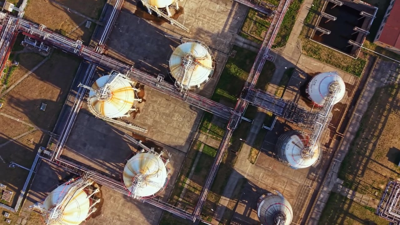 Oil storage tanks and pipes seen from above in an industrial area during daylight, illustrating infrastructure and operations in the location