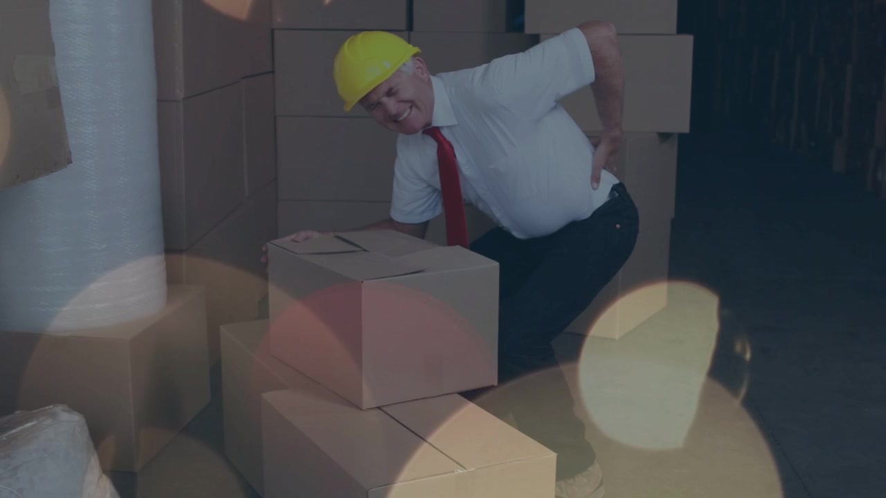 Trabajador apilando cajas en almacén, agachándose para levantar una caja y causando dolor de espalda bajo superposiciones bokeh.