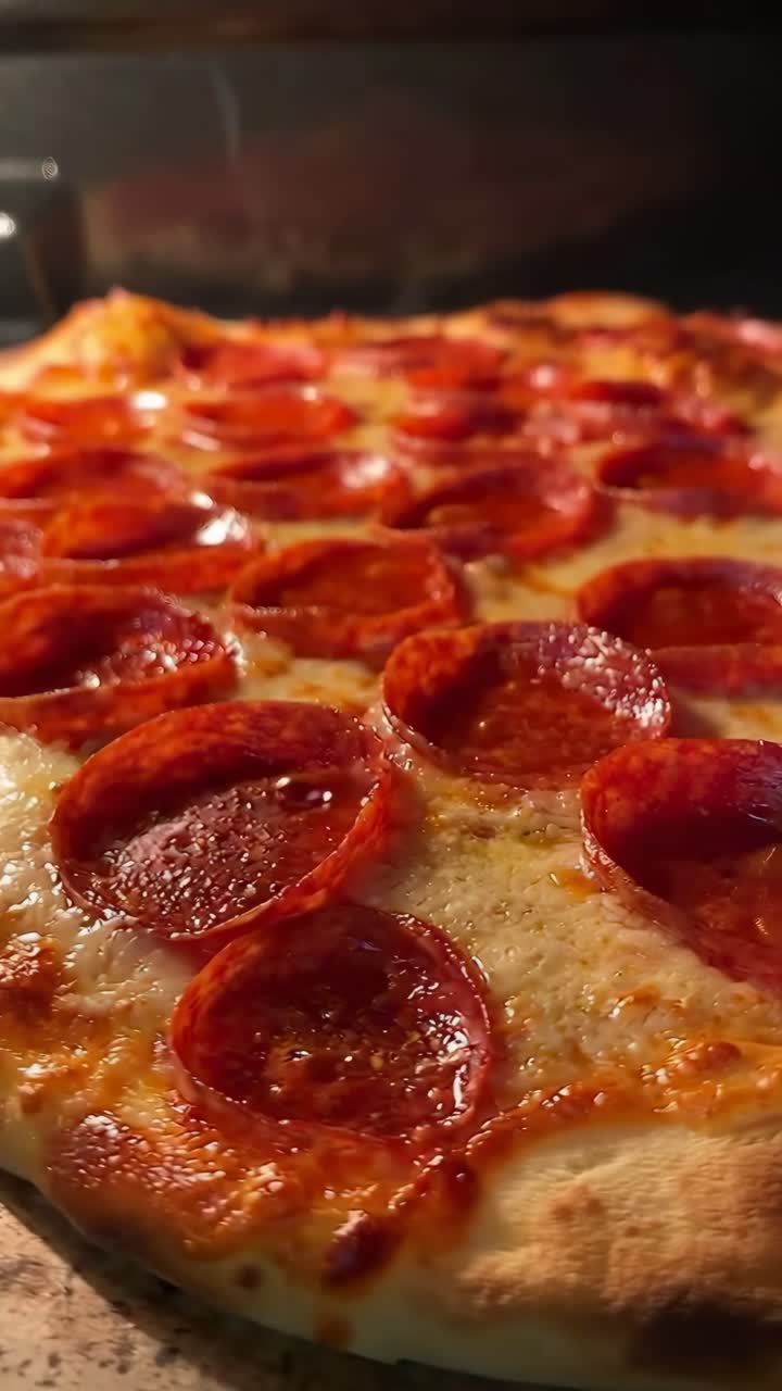 Video ravvicinato con angolazione della camera su una pizza ai peperoni in cottura, con formaggio fuso e condimenti in evidenza