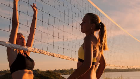 Cámara-Lenta,-ángulo-Bajo,-Primer-Plano,-Destello-De-Lente:-Jóvenes-Jugadoras-De-Voleibol-Pasan-Y-Rematan-La-Pelota-Sobre-La-Red-En-Una-Soleada-Tarde-De-Verano.-Chicas-Caucásicas-En-Forma-Jugando-Voleibol-De-Playa-Al-Atardecer.