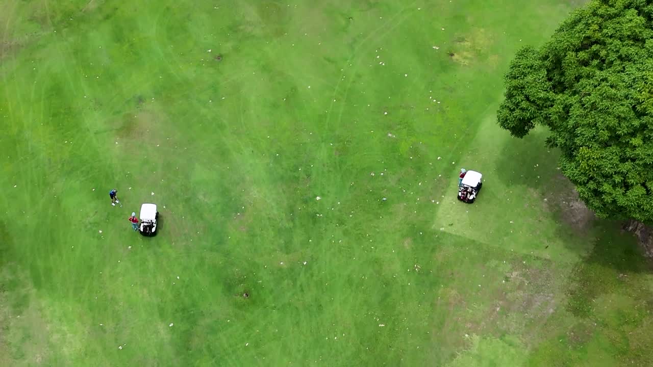 Drone captures a golf cart and lush green fairway with surrounding trees from above.