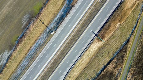 an overhead top-down drone shot of a highway in the winter with cars passing through the frame