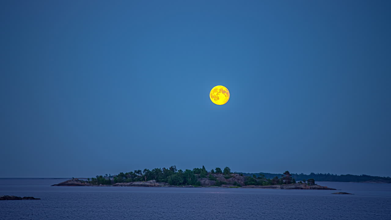 노란빛의 슈퍼보름달이 바다 위 외딴섬 위로 하늘로 뜬다.