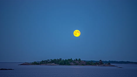 yellow-colored-super-full-moon-rises-up-to-sky,-over-remote-island-on-sea