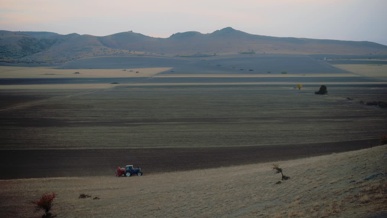 solo tractor que siembra o esparce fertilizantes en un gran campo agrícola en una mañana fría, desolada