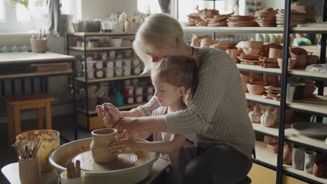 grandmother teaches her granddaughter working on a pottery rotating wheel