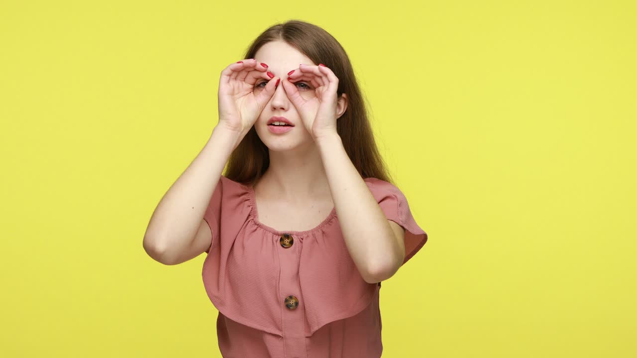 la mujer hace gafas con las manos, mira a través de los dedos.