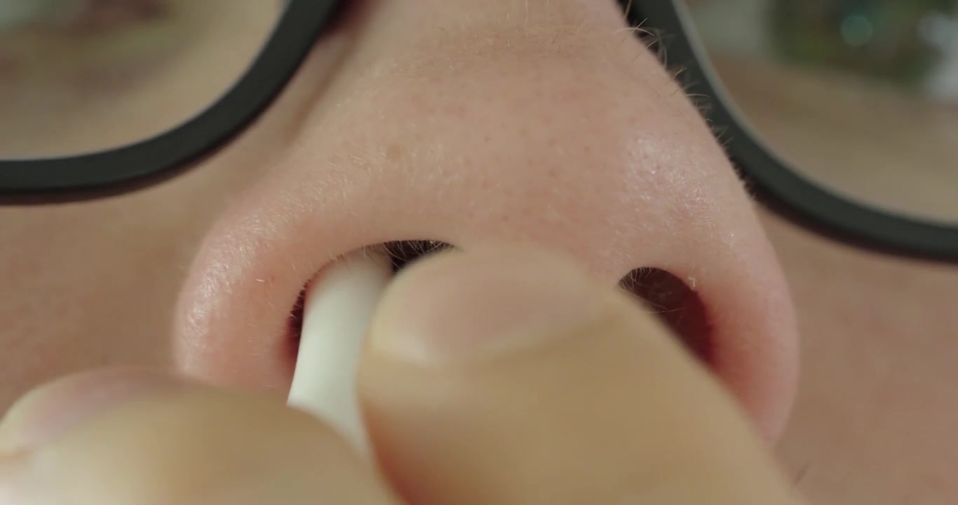 Primo piano macro estremo di una persona che applica spray nasale in una narice. Concetto di cura nasale, sollievo dalle allergie, trattamento della congestione, salute respiratoria, farmaci e assistenza sanitaria personale.