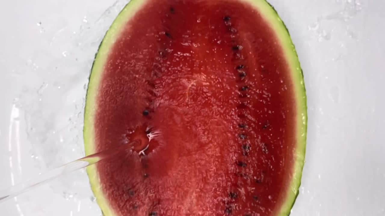 el chorro de agua cae sobre la sandía madura roja jugosa cortada por la mitad y cae en el spray