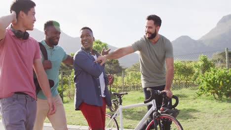 Felices-Amigos-Varones-Diversos-Caminando-Con-Bicicleta-Y-Hablando-En-Un-Día-Soleado