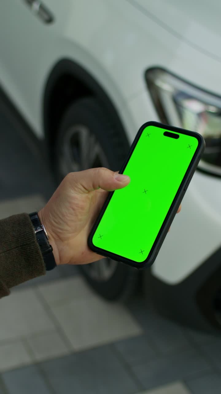persona sosteniendo un teléfono inteligente con una pantalla verde frente a un coche blanco