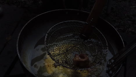 a spider strainer retrieving a fried dumpling from a large wok of hot oil