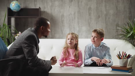 Little-girl-answers-nodding-tutor-and-classmate-sits-on-sofa