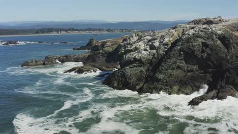 Stationary-aerial-drone-footage-of-crashing-ocean-waves-on-a-large-boulder,-which-sits-in-the-Pacific-ocean,-Oregon