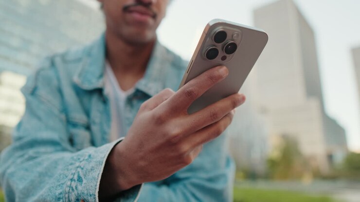 Young Man Smiling While Using Smartphone in Urban Park