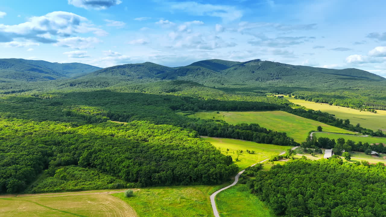 Lush green landscape with rolling hills. Vast green fields and woods stretch across the horizon beneath a bright blue sky on a sunny day