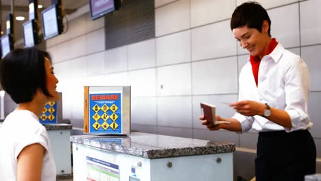 Personal-Femenino-Del-Aeropuerto-Revisando-El-Pasaporte-E-Interactuando-Con-Una-Mujer-En-El-Mostrador-De-Facturación.