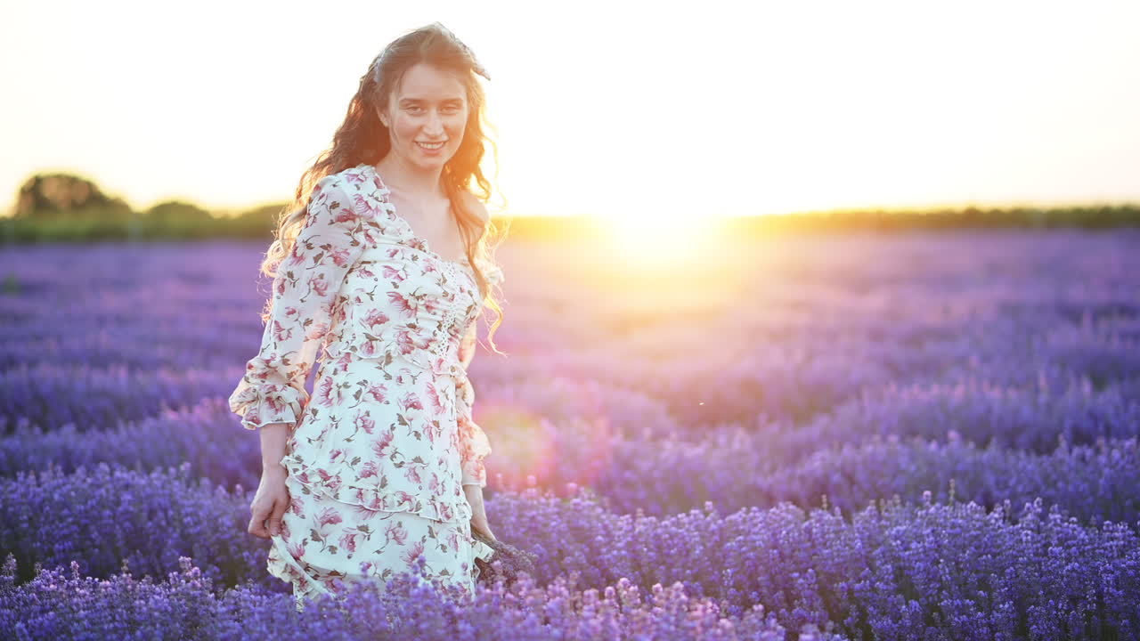 Beautiful woman walking through a lavender field, touching the flowers and smiling as the sun sets