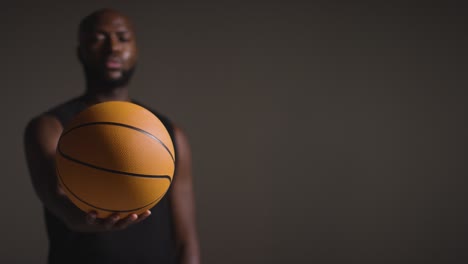 studio portrait shot of male basketball player holding ball towards camera