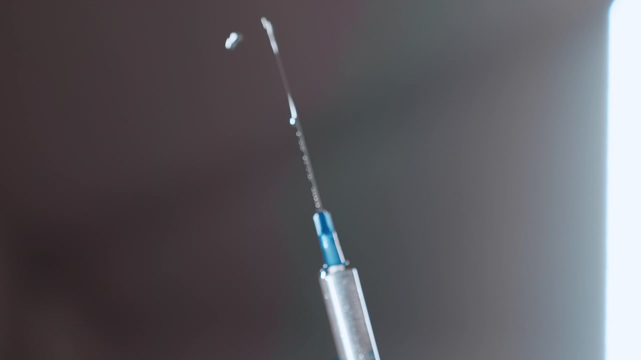 Closeup needle droplet on tip by black nurse, tiny fluid bead reflecting light, shallow depth of field, cool clinic lighting, careful inspection for air bubbles, steady hand technique, clinical focus