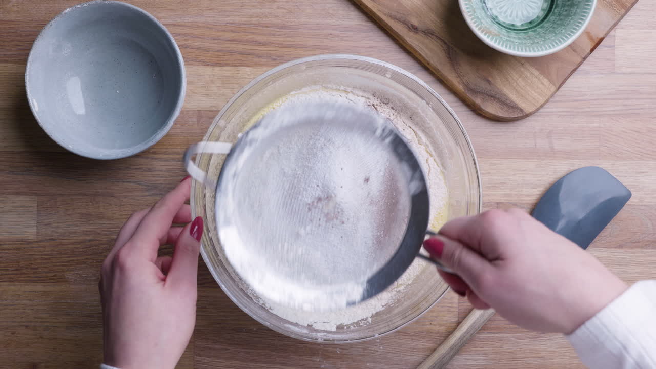 Mani femminili che setacciano ingredienti secchi in una ciotola.