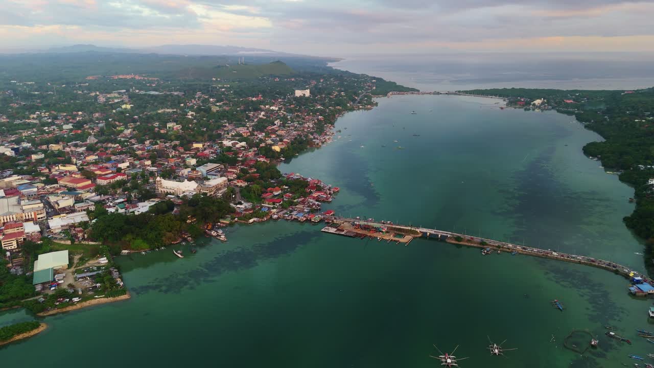 Panorama udara jembatan yang menghubungkan Bohol ke Pulau Panglao saat senja. Pemandangan pelabuhan Tagbilaran dan perairan tenang selat saat matahari terbenam tropis