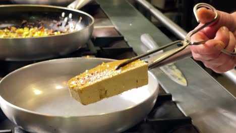 las pinzas de la cocina sosteniendo un pedazo de foie gras, colocándolo en una sartén caliente para broncearlo, cerrar