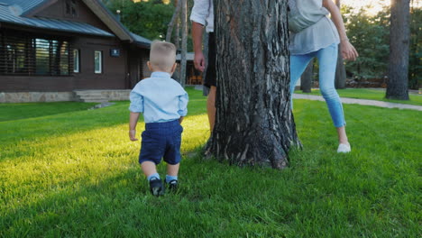 los padres felices juegan al escondite con un bebé que corre felizmente detrás de ellos alrededor del árbol feliz t