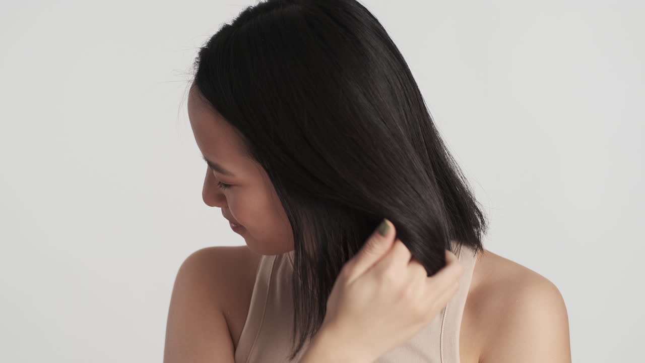 아시아 여성이 카메라 앞에서 머리를 고 있습니다.