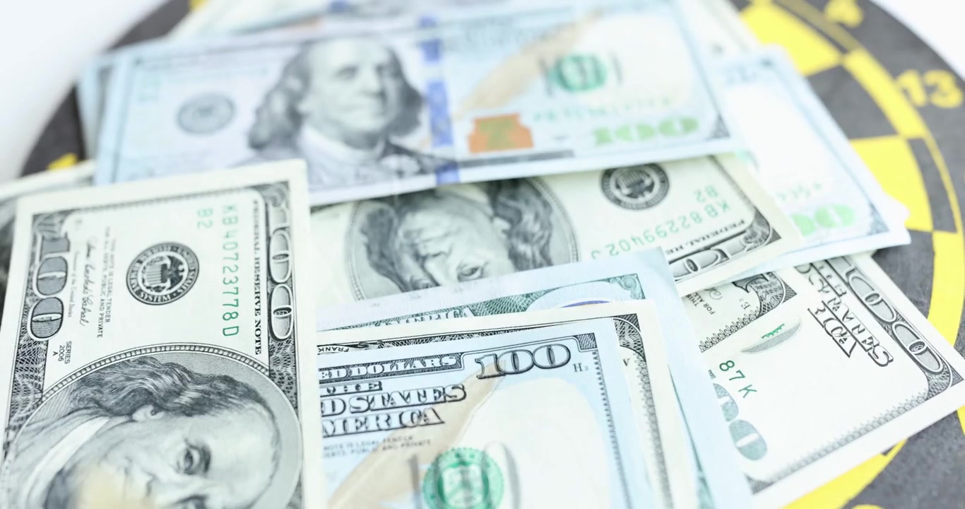 Banconote da cento dollari cadono su un bersaglio per freccette per scommettere sul vincitore