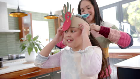 Happy-biracial-mother-and-daughter-playing-with-paper-band-and-smiling-in-sunny-living-room