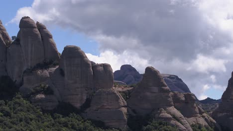 Striking-rock-formations-standing-between-green-shrubs,-blue-sky-and-clouds