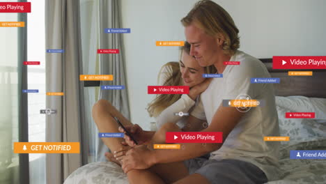múltiples iconos digitales sobre una pareja caucásica usando un teléfono inteligente juntos en la cama en casa