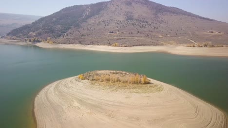 A-trucking-pan-of-an-island-attached-to-a-dry-lake-bed-with-aspen-trees-and-a-bright-blue-sky