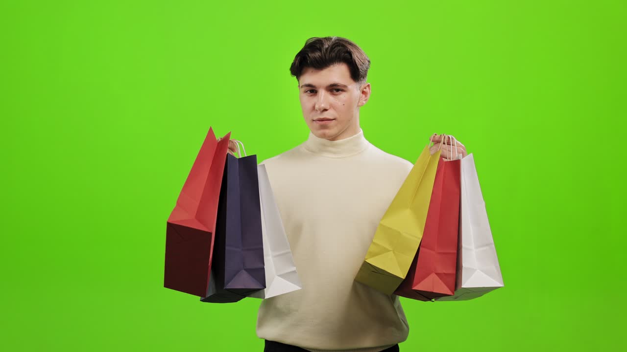 남자는 카메라를 바라보고 쇼핑 가방을 집어 들고 있습니다. 그는 피곤하고 감정적이지 않습니다. 그는 녹색 배경에 서 있습니다. 녹색 화면.