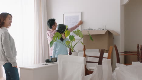 Glückliche-Asiatische-Familie,-Die-In-Ein-Neues-Haus-Zieht,-Eigentümer-Hängen-Bilder-Auf,-Die-Das-Haus-Zusammen-Mit-Kindern-Dekorieren.-Junges-Paar-Genießt-Immobilieninvestitionen-Mit-Kindern,-4K-Videos