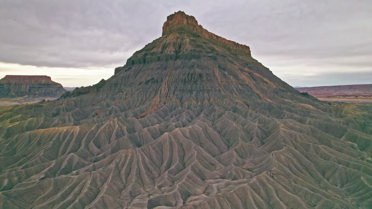 Stunning 4K drone footage of Utah’s Factory Butte, showcasing dramatic striated slopes, layered sedimentary rock formations, and the raw beauty of the desert landscape.