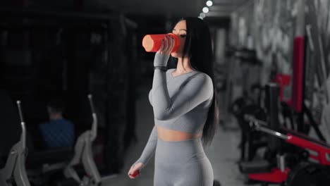 chica atlética con curvas en un traje deportivo bebe de una coctelera