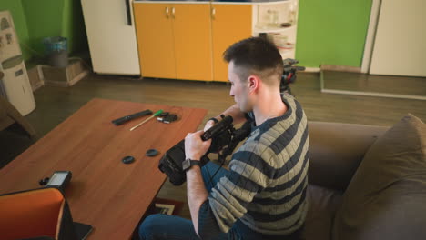 person seated at desk with camera gear, adjusting camera lens. table with camera, microphone, smartphone, bag. modern workspace, indoor setup, photography equipment, tech tools